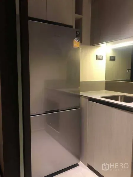Condominium for rent in Watthana, Bangkok - Stainless steel refrigerator next to sink and cabinets in a compact condo kitchen.