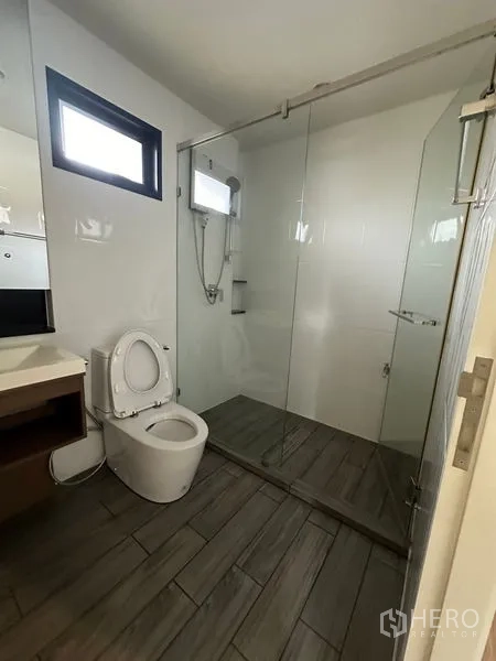 บ้าน ให้เช่าหรือขายในLam Luk Ka, Pathum Thani - ห้องน้ำมีตู้กระจกกั้นอาบน้ำ ผนังสีขาว และพื้นลายไม้สีเทา