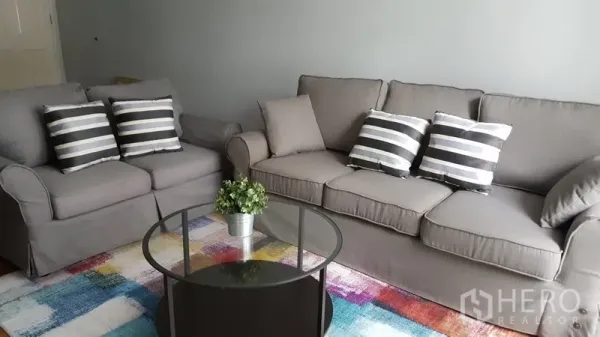 คอนโด ให้เช่าในWatthana, Bangkok - ห้องนั่งเล่นสไตล์อบอุ่น โซฟาสีเทาสองตัว หมอนลายทาง โต๊ะกลางกระจก และพรมสีสัน