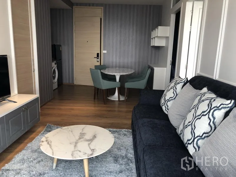 Condominium for rent in Khlong Toei, Bangkok - Open-plan living area with navy sofa, marble coffee table, and wood floors.