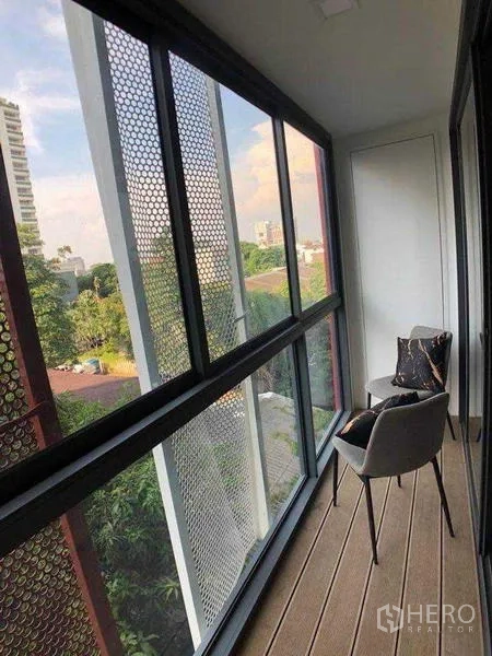 คอนโด ให้เช่าในWatthana, Bangkok - ระเบียงปิดพื้นไม้ พร้อมเก้าอี้สองตัว มองเห็นต้นไม้และอาคารรอบข้าง