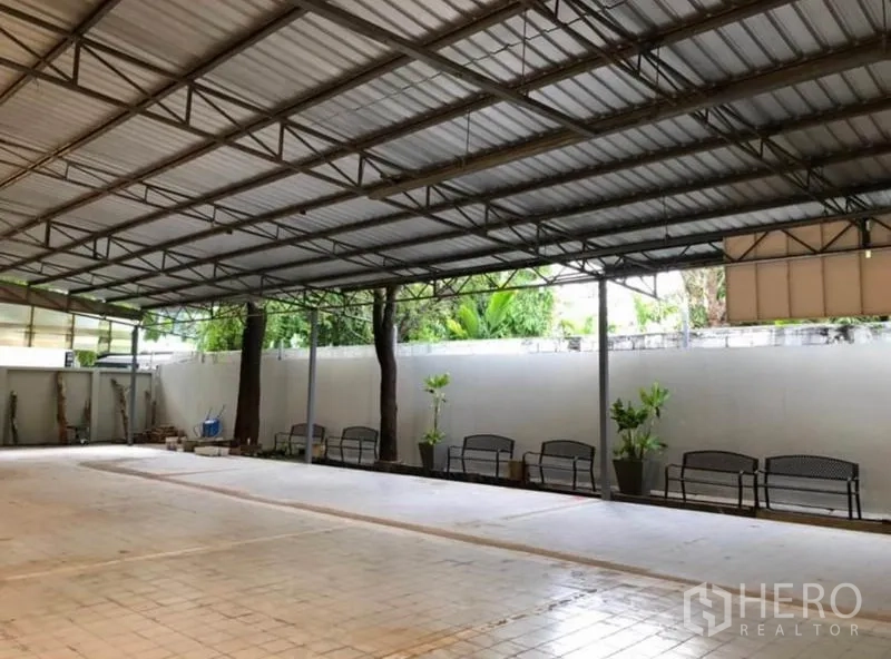 คลังสินค้า ให้เช่าในKhlong Toei, Bangkok - โซนคลุมหลังคาร่มรื่น มีม้านั่ง ต้นไม้ และหลังคาโลหะเปิดข้างกำแพง