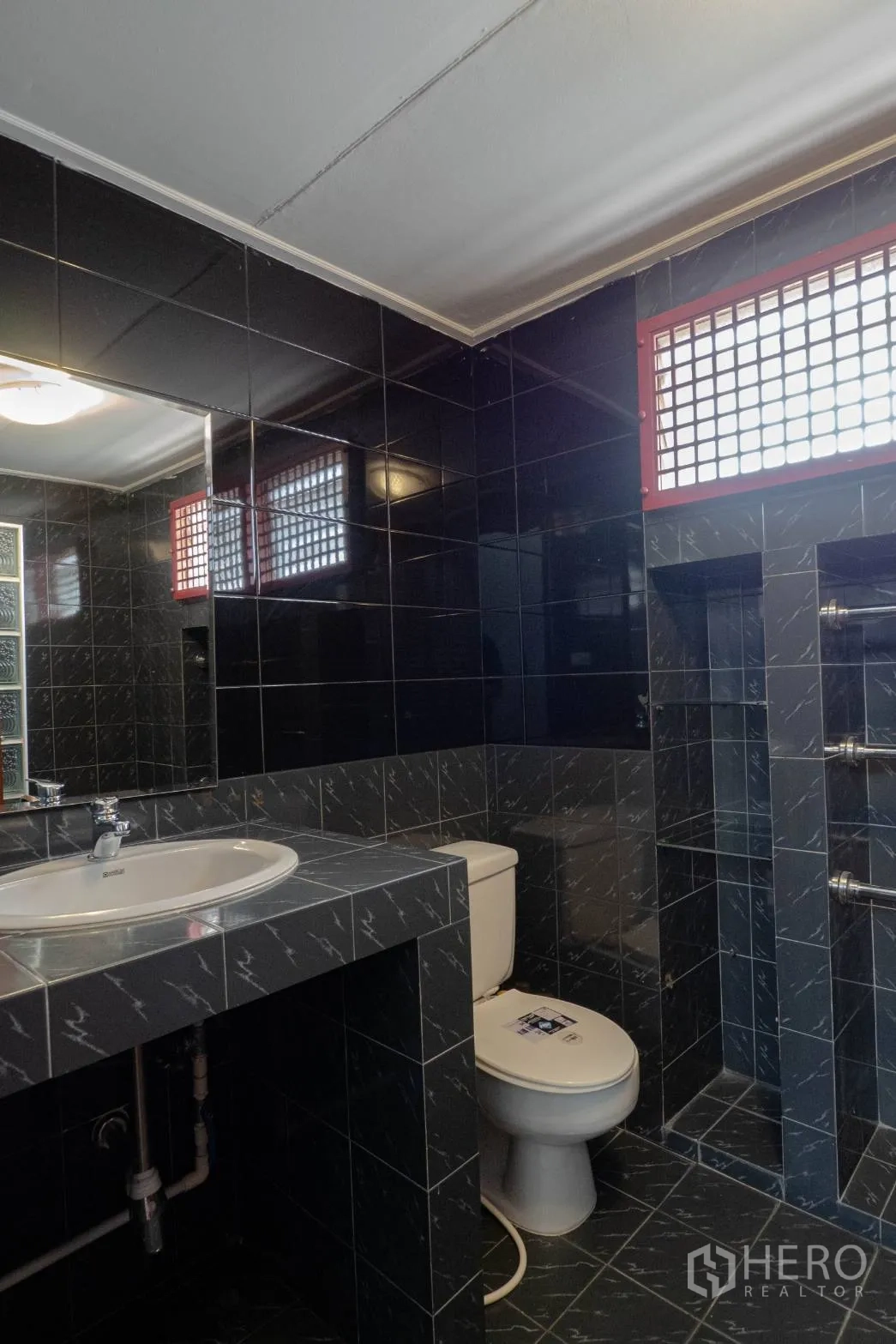 Townhouse for rent in Khlong Toei, Bangkok - Dark-tiled bathroom with sink, toilet and lattice vent window.