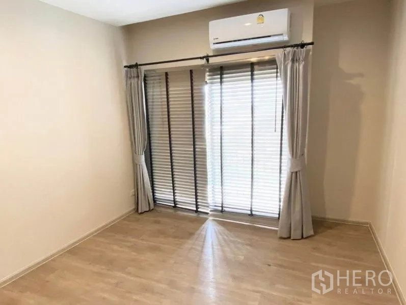 Condominium for rent in Pathum Wan, Bangkok - Second bedroom with air conditioner, wood floors and window with blinds and curtains.