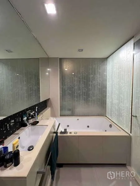 公寓 出租在Bang Rak, Bangkok - 浴室配台盆与按摩浴缸，旁有磨砂玻璃