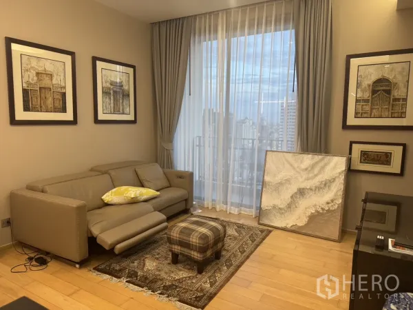 Condominium for rent in Watthana, Bangkok - Cozy living room with leather sofa, framed art, wood floors and floor-to-ceiling window with city view.