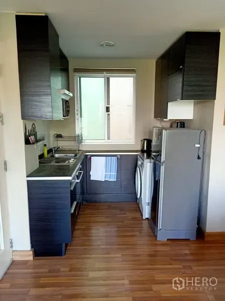 คอนโด ให้เช่าในKhlong Toei, Bangkok - ครัวแบบแกลเลย์ตู้สีเข้ม มีหน้าต่าง อ่างล้างจาน ตู้เย็น และเครื่องซักผ้าบนพื้นไม้