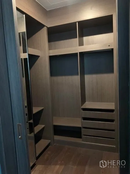 Condominium for rent in Watthana, Bangkok - Walk-in closet with built-in shelves, drawers and a full-height mirror in dark wood finish.