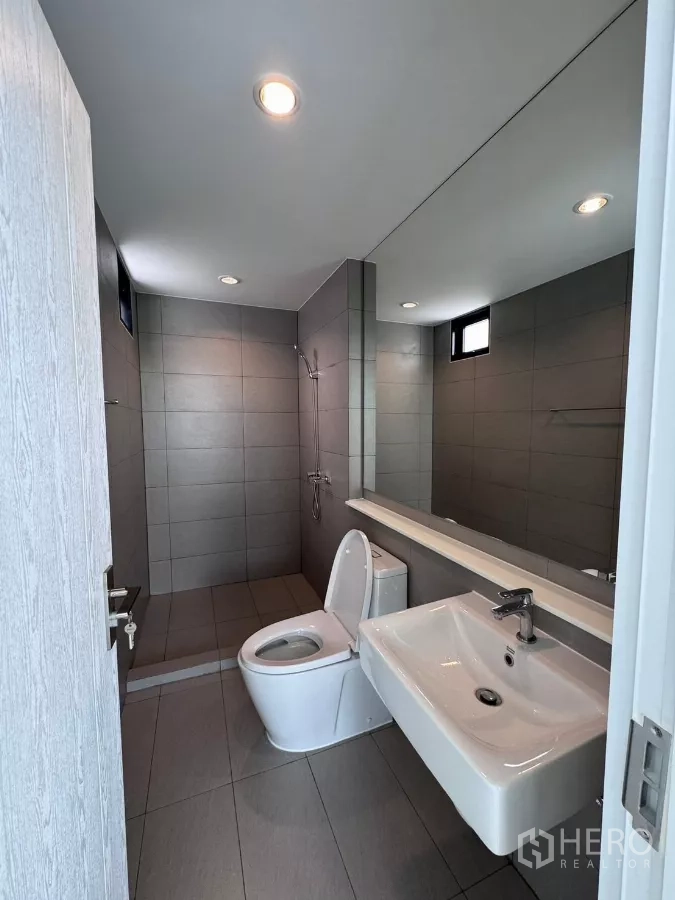 Detached House for rent in Samut Prakan - Second bathroom with gray tiles, walk-in shower and long mirror.
