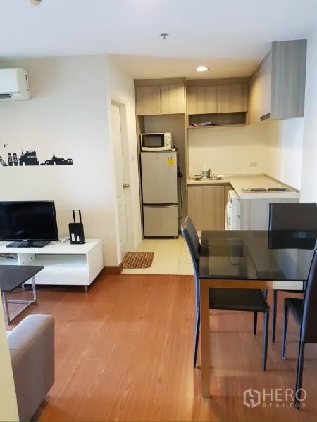 Condominium for rent in Huai Khwang, Bangkok - Open-plan living room with dining table and compact kitchenette on wood floors.