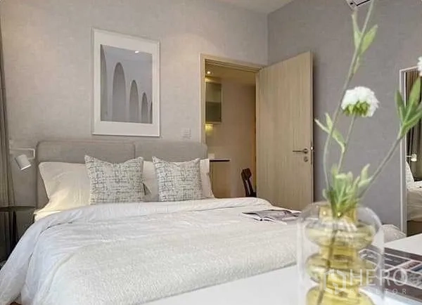 Condominium for rent in Watthana, Bangkok - Cozy bedroom with double bed, soft linens and wall art, with door open to hallway and a small vase in foreground.