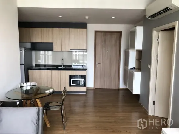 Condominium for rent in Watthana, Bangkok - Open-plan kitchen with wood cabinets, black countertop, glass splashback, fridge and round glass dining table.