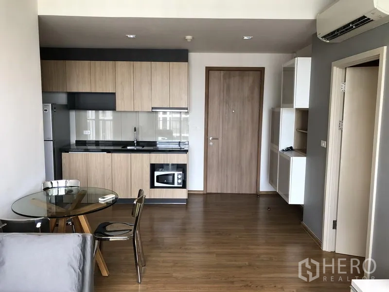 Condominium for rent in Watthana, Bangkok - Open-plan kitchen with wood cabinets, black countertop, glass splashback, fridge and round glass dining table.