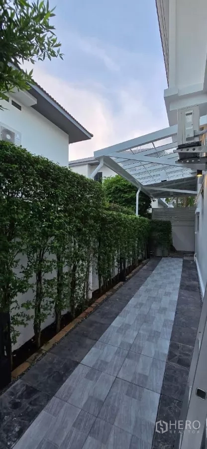 Detached House for rent in Samut Prakan - Tiled side walkway with canopy and hedge screening.