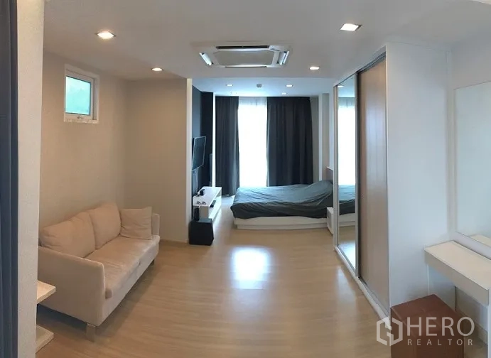 Condominium for sale in Khan Na Yao, Bangkok - Open-plan bedroom and living area with sofa, platform bed, mirrored wardrobe, TV and floor-to-ceiling windows.