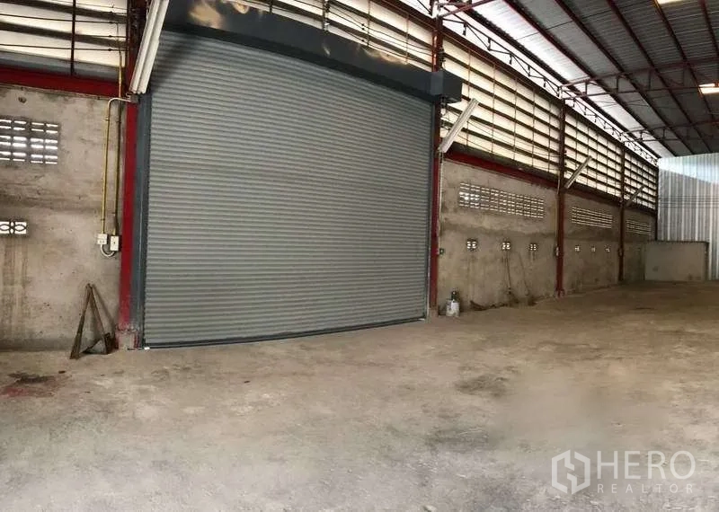 Warehouse for rent in Phra Pradaeng, Samut Prakan - Large interior roll‑up shutter door with ventilation block walls and metal roof ideal for truck loading.