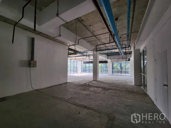 Retail Space for rent in Sathon, Bangkok - Open-plan retail area with large windows, blue overhead pipes and raw concrete slab.