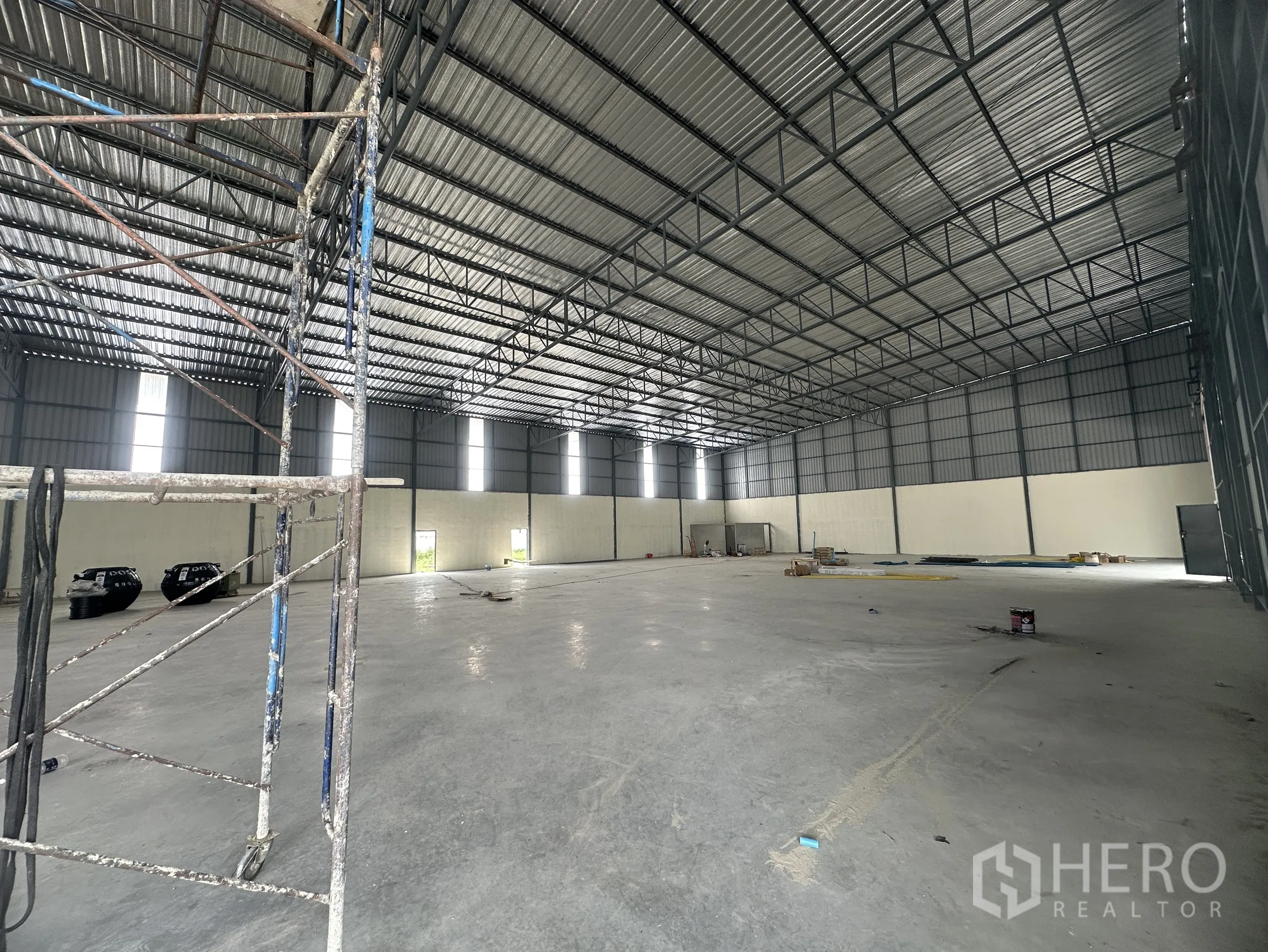 Warehouse for rent in Lam Luk Ka, Pathum Thani - Wide interior space with scaffolding, polished floor, and multiple high windows.