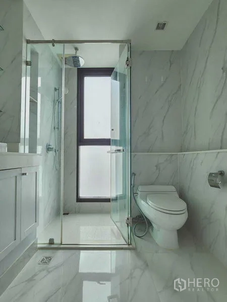 公寓 出租在Bang Rak, Bangkok - 明亮的白色大理石风浴室，玻璃淋浴间与采光窗。