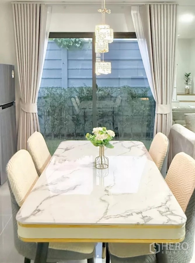 Townhouse for rent in Bang Phli, Samut Prakan - Marble-top dining table under crystal pendant lights facing the yard.