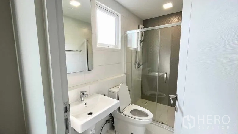 Detached House for rent or sale in Prawet, Bangkok - Modern bathroom with glass shower enclosure, window and white fixtures.
