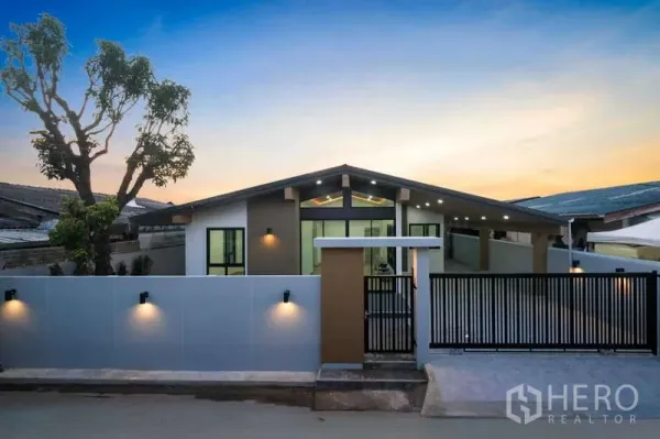 独立式住宅 出售在Bueng Kum, Bangkok - 街景角度的当代立面，围墙与金属大门，墙面照明映衬黄昏