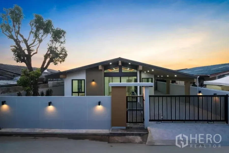 独立式住宅 出售在Bueng Kum, Bangkok - 街景角度的当代立面，围墙与金属大门，墙面照明映衬黄昏