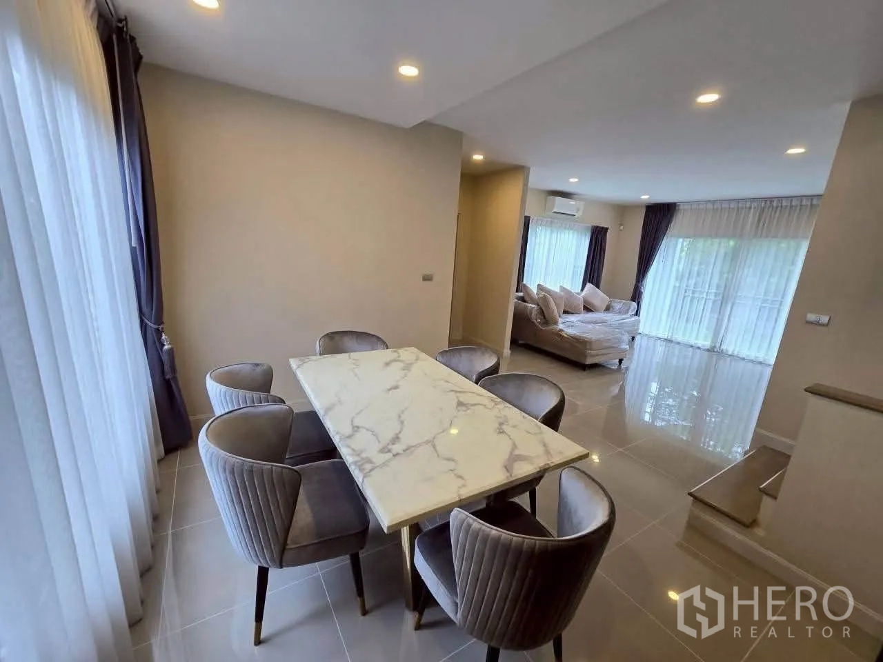 Detached House for rent or sale in Lat Krabang, Bangkok - Dining space opening to living room with sofa and wide windows.