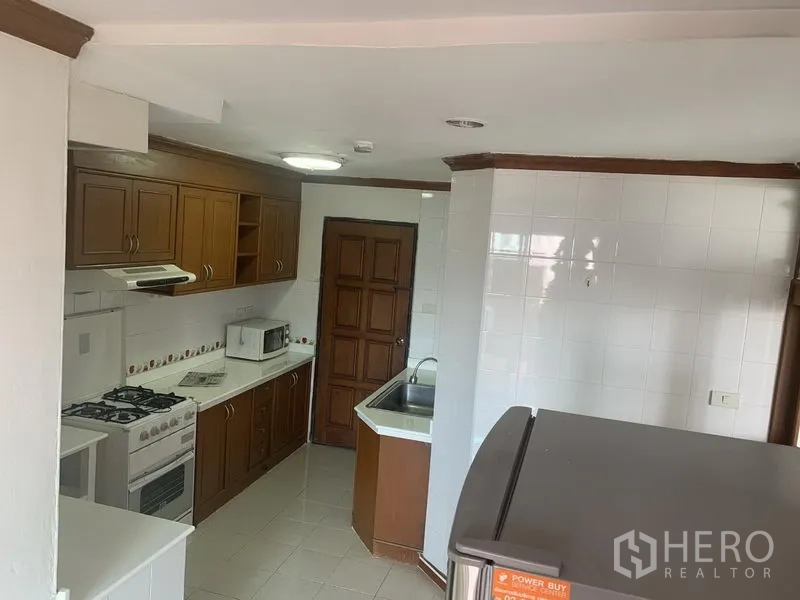 Condominium for rent in Watthana, Bangkok - Wide kitchen view showing double sink, microwave, tiled floors and a door to the utility area.