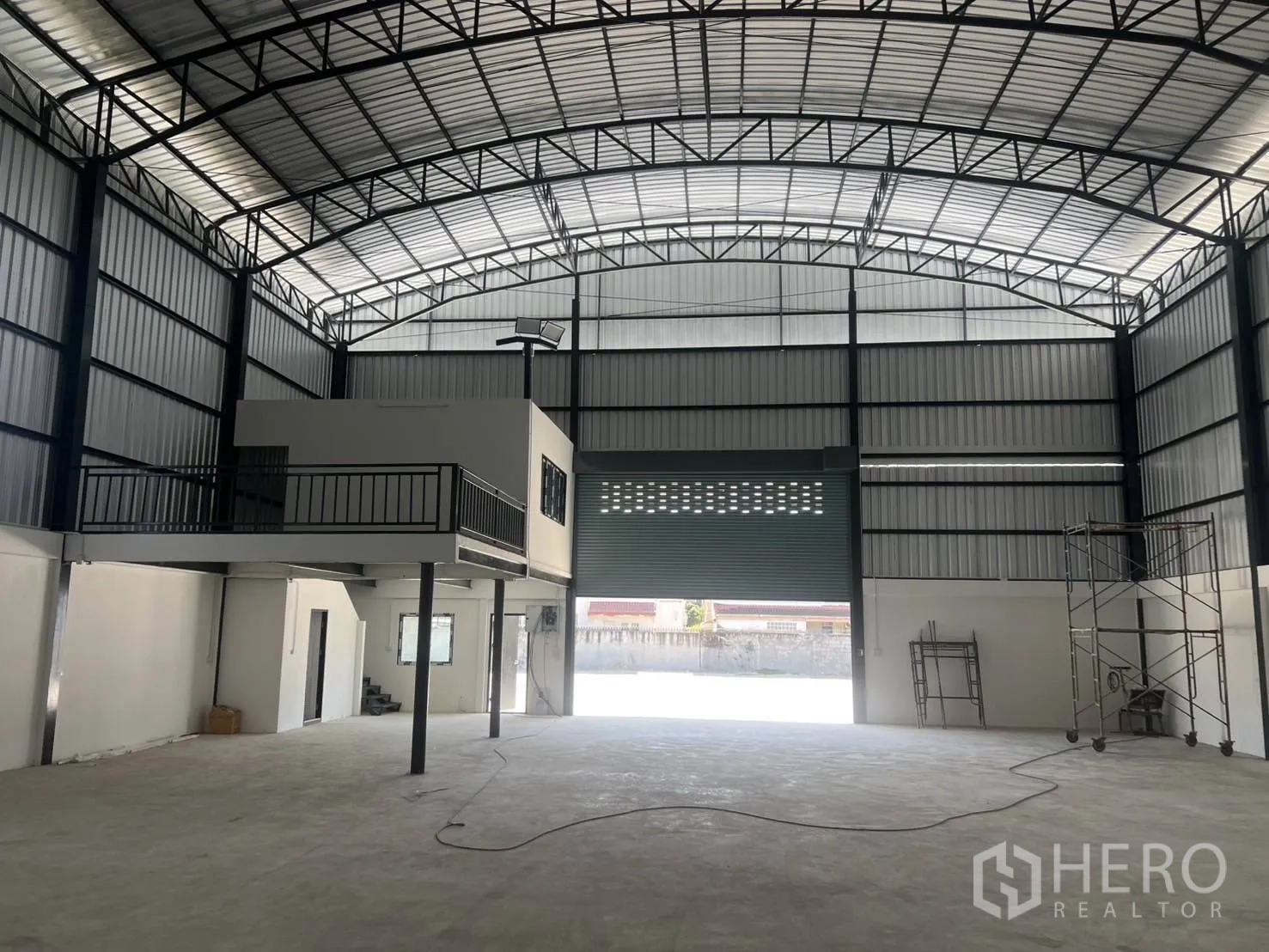 Warehouse for rent in Bang Phli, Samut Prakan - View toward the wide roller shutter entry with mezzanine on the side and scaffolding in the open space.