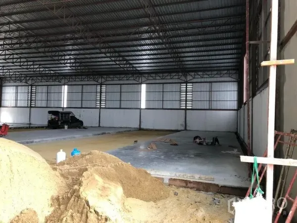 Warehouse for rent or sale in Sai Noi, Nonthaburi - Open warehouse bay with corrugated metal walls and partially poured concrete flooring.