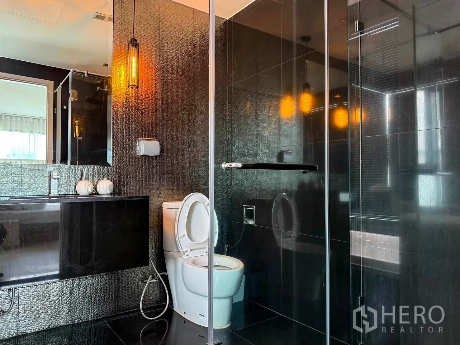Condominium for rent in Khlong Toei, Bangkok - Bathroom featuring glass shower, pendant lighting, and textured dark tiles.