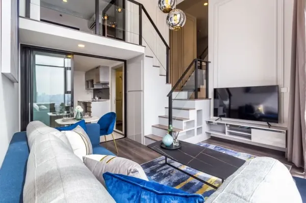 Condominium for rent or sale in Chatuchak, Bangkok - Loft-style living room with staircase, TV console and open connection to the kitchen and dining area.