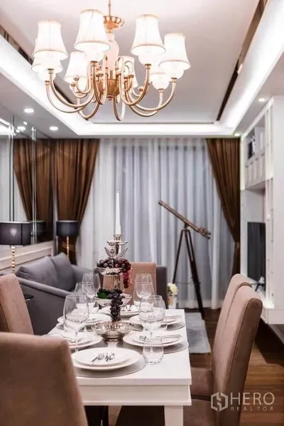 Condominium for rent in Huai Khwang, Bangkok - Elegant dining table under a chandelier with curtained glass doors and a telescope beside the living area.