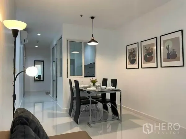 Condominium for rent or sale in Watthana, Bangkok - Open dining area with four-seat glass table, pendant light and wall art beside corridor.