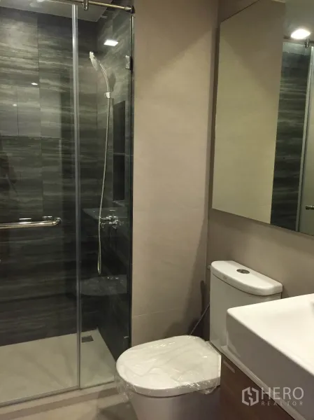 คอนโด ให้เช่าในPathum Wan, Bangkok - ห้องน้ำสมัยใหม่พร้อมตู้ชาวเวอร์กระจก ฝักบัว กระจกบานใหญ่ และโถสุขภัณฑ์ โทนสีอบอุ่น