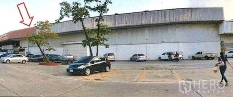 Warehouse for rent in Phra Pradaeng, Samut Prakan - Long metal-clad warehouse facade with loading bays, tree-lined parking and clear truck access.
