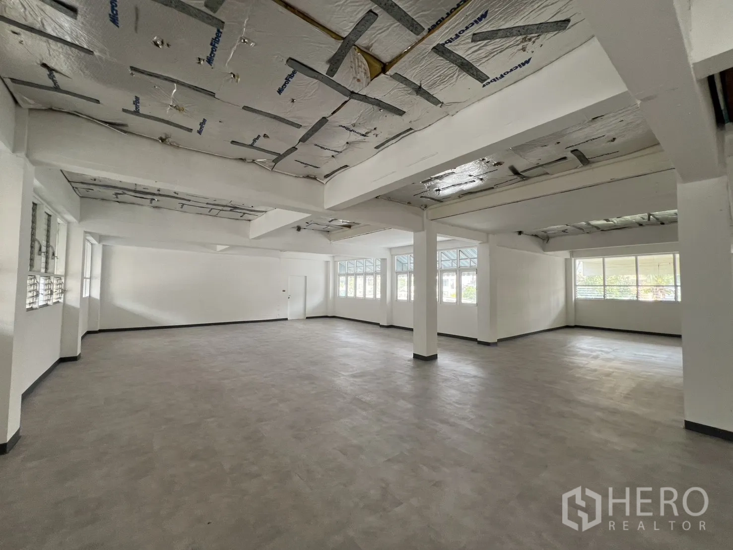 办公空间 出租在Watthana, Bangkok - 素坤逸开放式办公楼层，灰色地面、承重柱与两侧大窗采光。