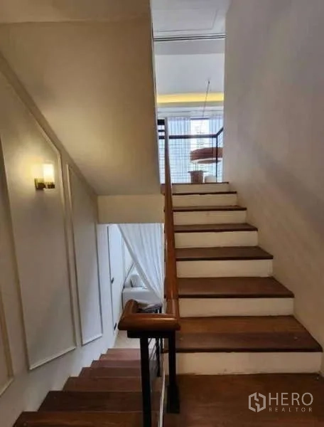 Townhouse for rent - Staircase with wood treads and a wall sconce leading toward a mezzanine area.