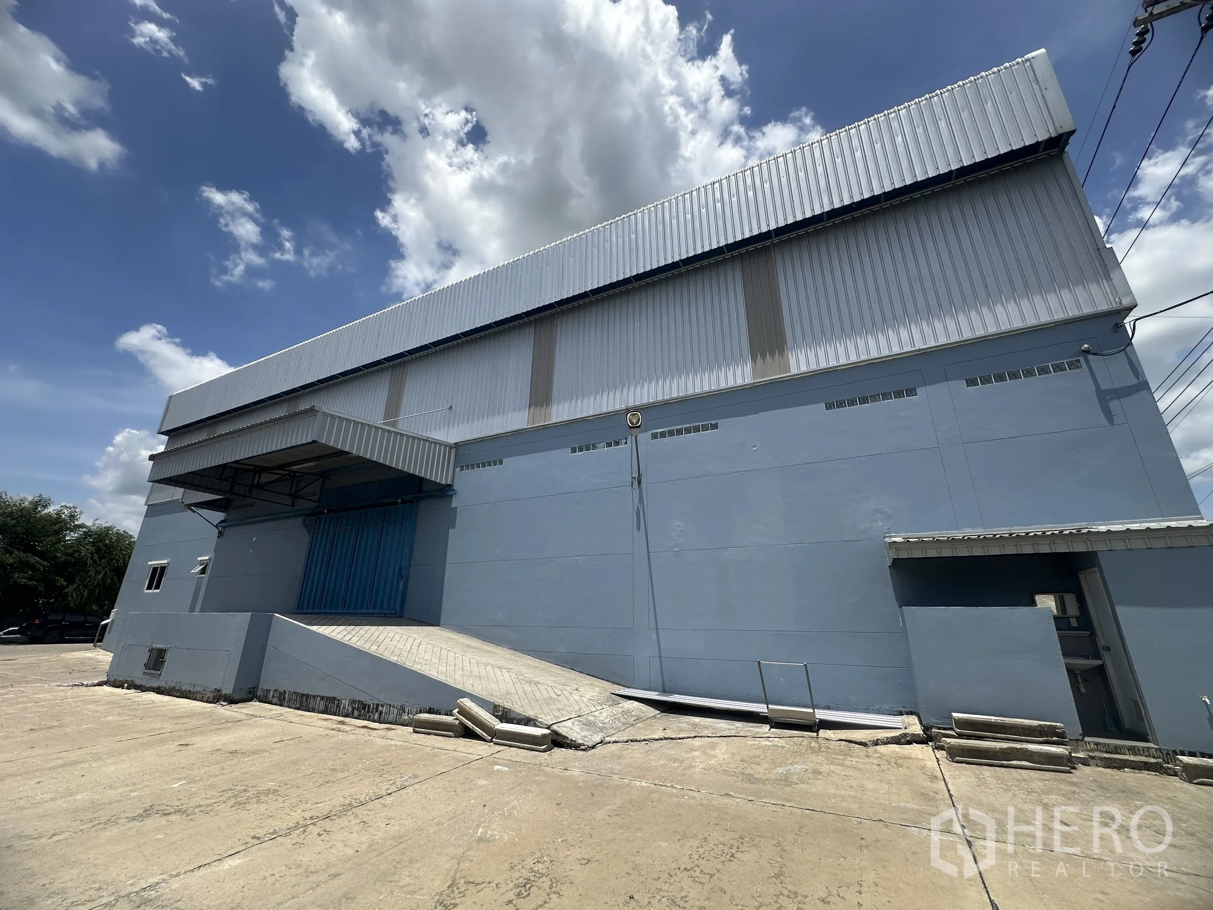 Warehouse for rent in Lat Lum Kaeo, Pathum Thani - Exterior of warehouse with ramp access to a loading door and concrete yard for trucks.