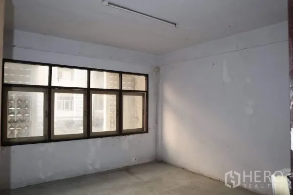 Shophouse for sale in Huai Khwang, Bangkok - Upper-floor room with large windows and plain white walls ready for renovation.