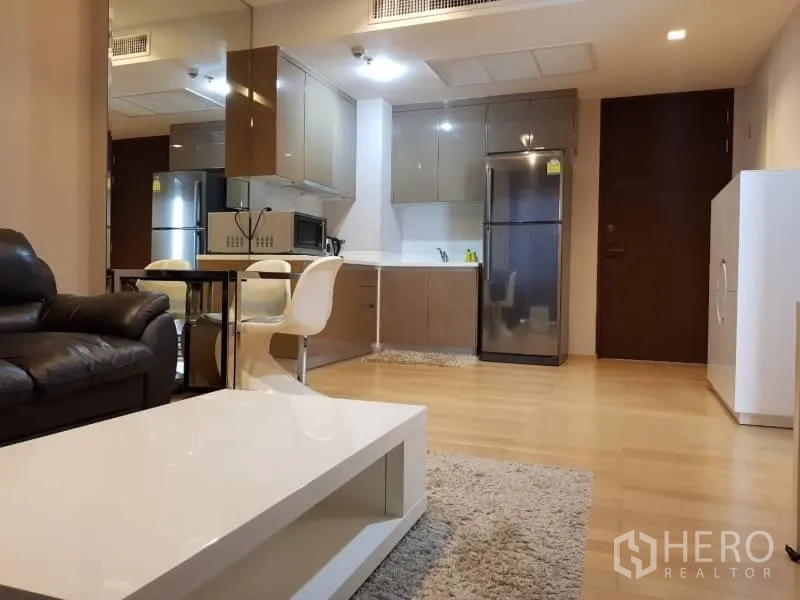 Condominium for rent in Khlong Toei, Bangkok - Fitted kitchen with upper cabinets, stainless refrigerator, dining table, and adjoining living space.