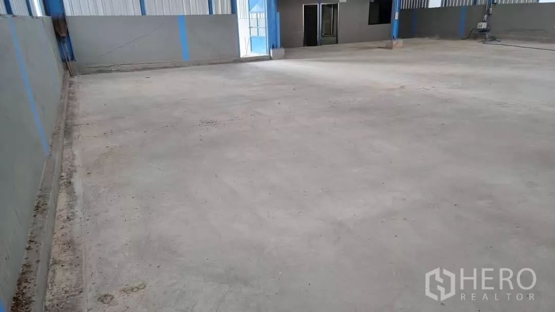 Warehouse for rent in Min Buri, Bangkok - Open-plan warehouse interior with high clearance and smooth concrete floor leading to an office entry.