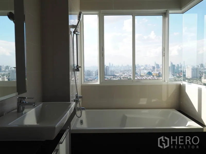 Condominium for rent in Yan Nawa, Bangkok - Bathroom with a large soaking tub beneath wide windows showing Bangkok skyline and river, plus a vanity.