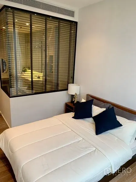 Condominium for rent in Pathum Wan, Bangkok - Cozy bedroom with double bed and glass-partitioned bathroom with blinds.
