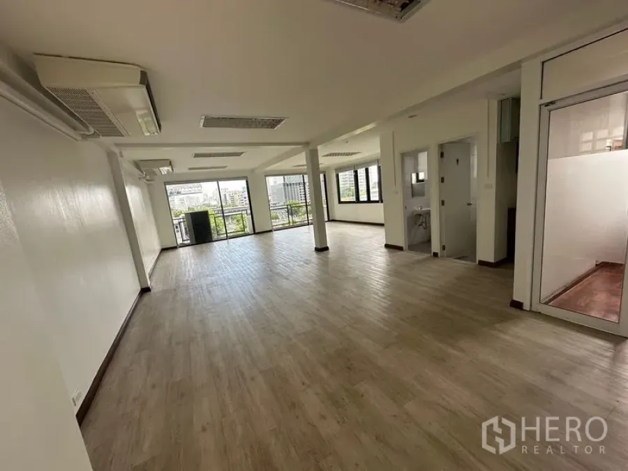 Office Space for rent in Sathon, Bangkok - Open-plan office interior with wood-look flooring, column support, large sliding glass doors to a balcony, ceiling lights, air-conditioning, and city views.