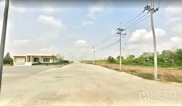 Land for sale in Lam Luk Ka, Pathum Thani - Wide 16‑meter concrete road with overhead power lines and a low‑rise office beside cleared industrial land in Lam Luk Ka.