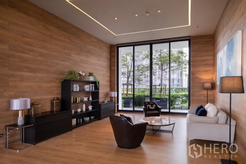 คอนโด ให้เช่า - เลานจ์ส่วนกลางผนังไม้ มีชั้นวางและหน้าต่างสูงติดสวน