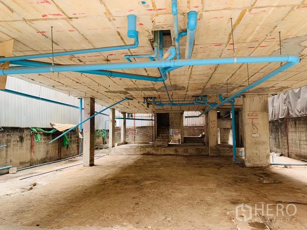 Home Office for rent - Ground level open space with concrete columns and extensive blue plumbing lines.