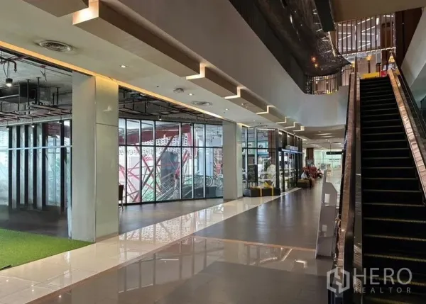 零售空间 出租在Watthana, Bangkok - 商场走廊，扶梯旁带玻璃立面的店铺与亮面地砖